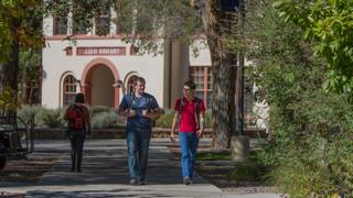 Two students are talking and walking towards the viewer, Cramer Hall can be seen in the background.